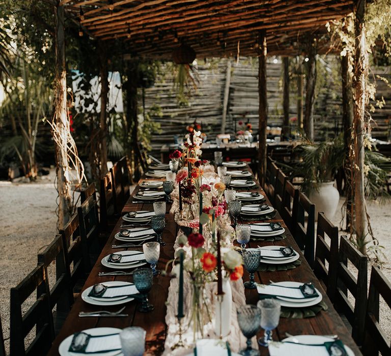 Outdoor wedding venue with dark wooden tables, white plates and green napkins and wedding stationery