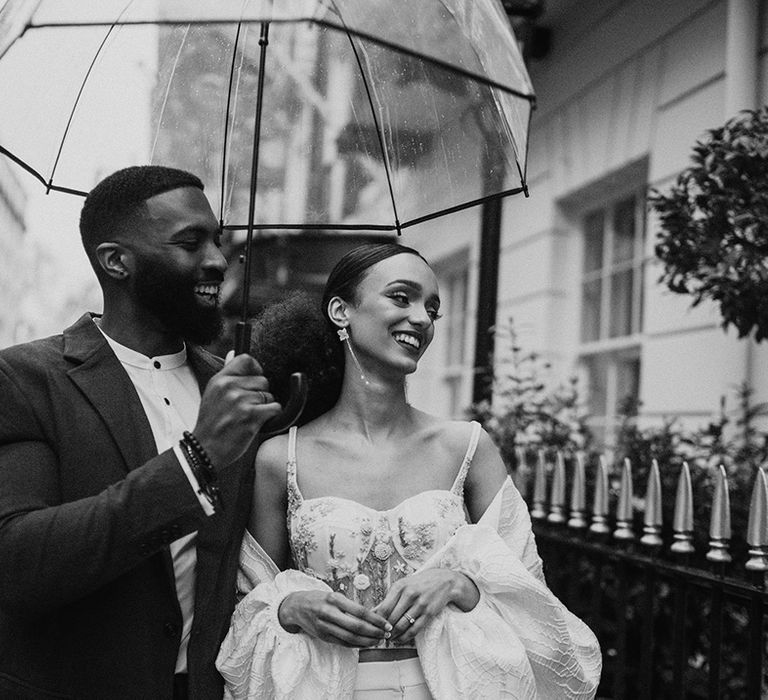 Black bride and groom standing under a clear umbrella at their intimate city wedding 