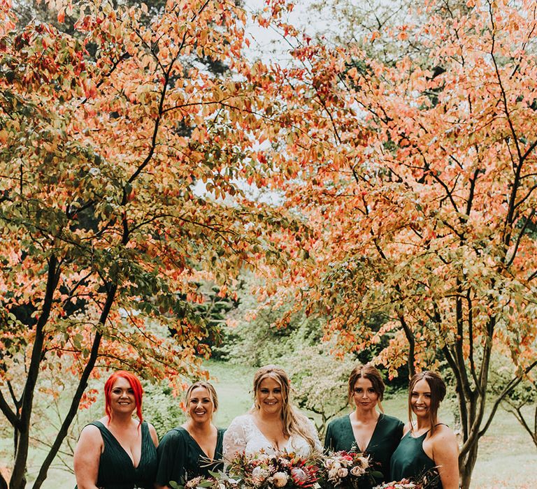 Bridal party in forest green bridesmaid dresses holding king protea and foliage bouquets 