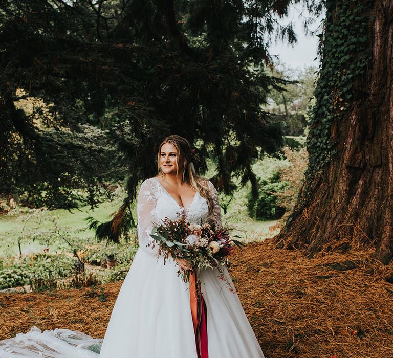 Curvy bride in a White Rose Bridal princess wedding dress with customised long lace sleeves holding an autumnal bouquet tied with burgundy ribbon 