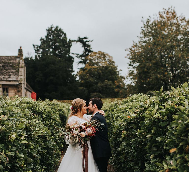 Bride in a lace princess wedding dress and groom in a navy suit embracing in the gardens at Askham Hall 