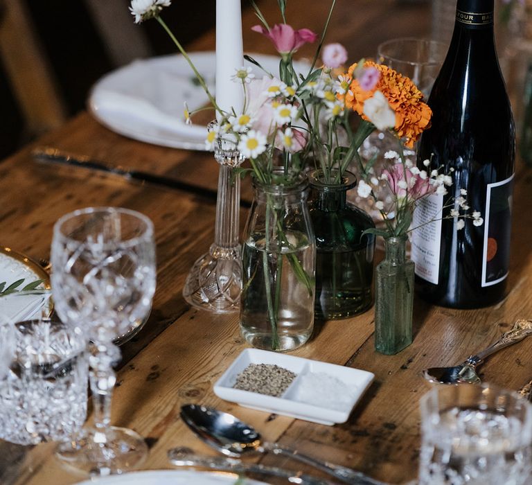 Tall white tapered candle in glass holder with small vases and minimal styled flowers for table setting 