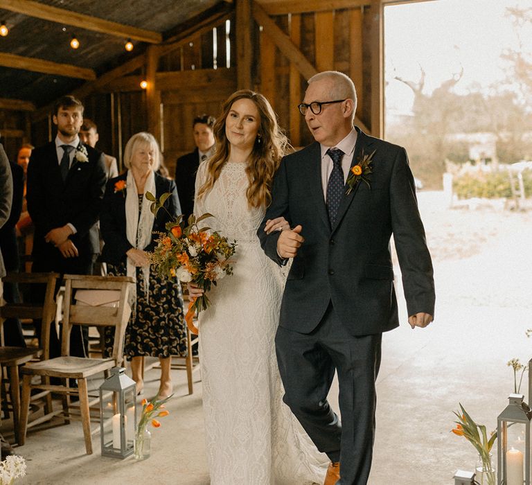 Tall silver lanterns with candles in decorate the aisle as father of the bride walks the bride down the aisle 