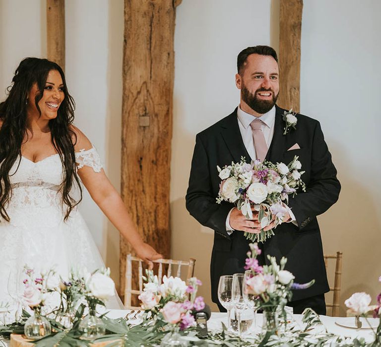 Bride in off the shoulder lace wedding dress and groom wearing pink tie stand up as they enter their reception 