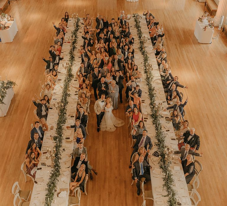 Bride in ruffle wedding dress with a long train walks with groom in custom tuxedo around their wedding venue in London 