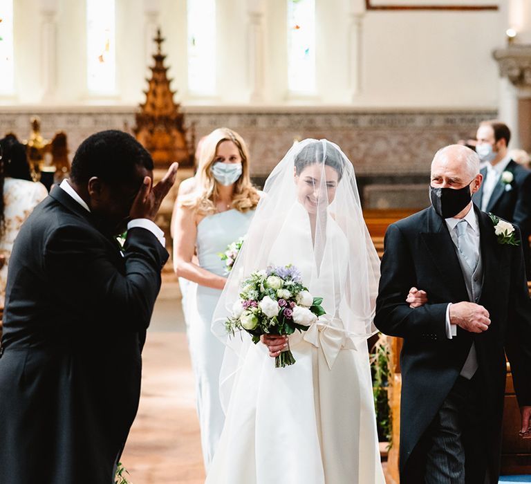 Groom wipes his tears as the bride is walked down the aisle by her father in three piece suit with baby blue tie