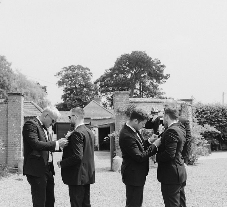 Groomsmen help each other fix on their dried flower buttonholes