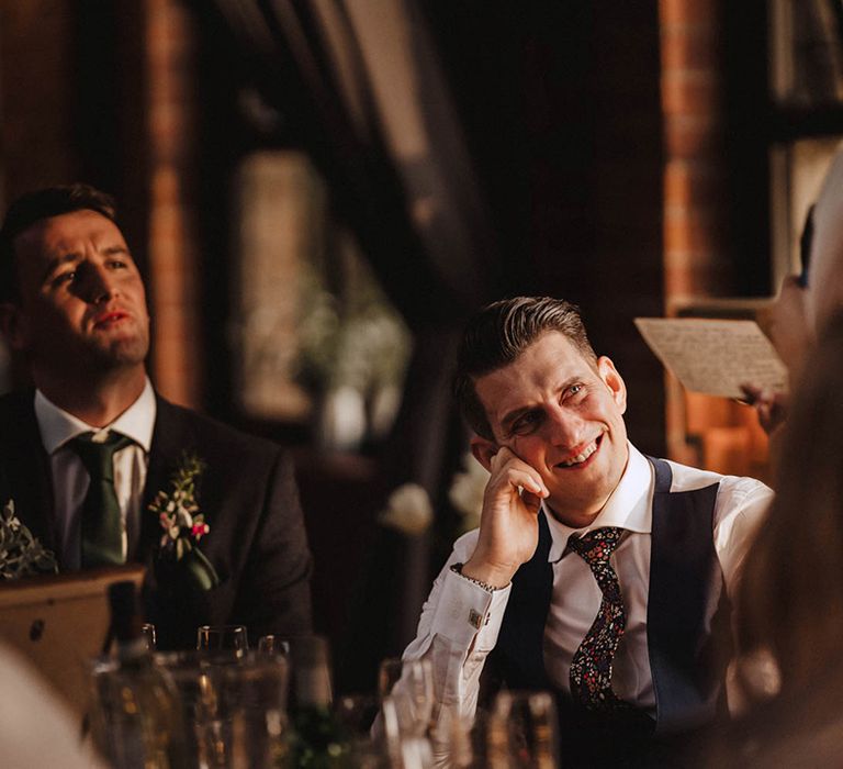 Groom smiles and looks up at the bride lovingly as she reads out her wedding speech 