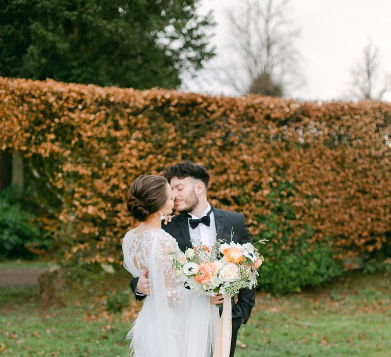 Groom in a tuxedo kissing his bride in a an applique wedding dress in the gardens at Holesfoot, Cumbria  