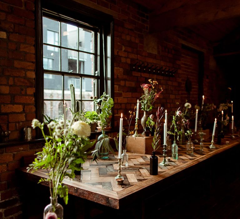 Rustic styling at The Chimney House complete with wild florals in differing sized vases on wooden table in front of industrial window