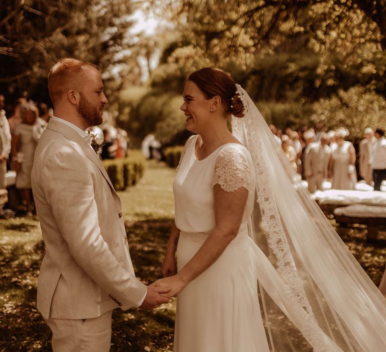 Bride veil blows in the wind behind her complete with lace edging as she looks at her groom outdoors in Spain