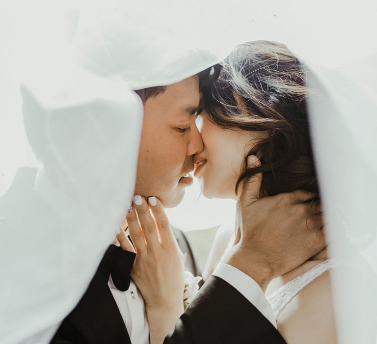 Bride & groom kiss beneath pearl veil 