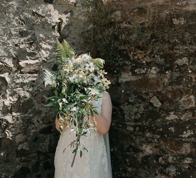 Bride holds up oversized floral bouquet filled with foliage and daisies 