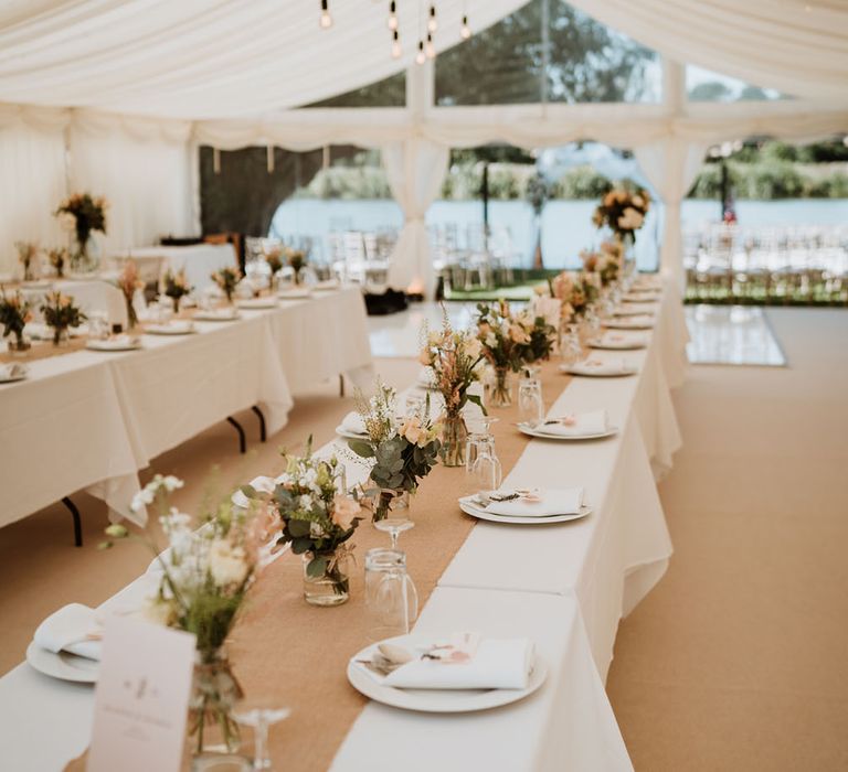 Marquee wedding reception complete with hessian table runner, small floral arrangement centrepieces and festoon lighting 