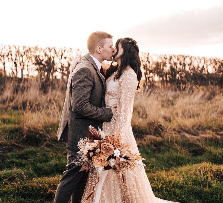 Bride in gold wedding dress kisses her groom outdoors on their wedding day for couples portraits