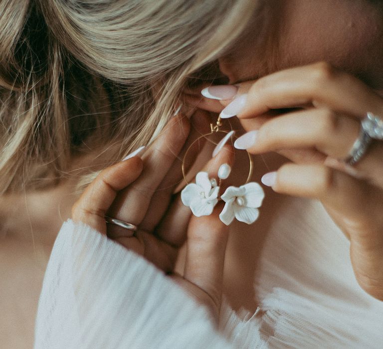 Bride putting in gold hoop earring with small dainty white rose and pearl detail in the middle