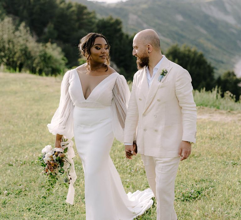 Bride and Groom walk hand in hand through fields on the Italian coast