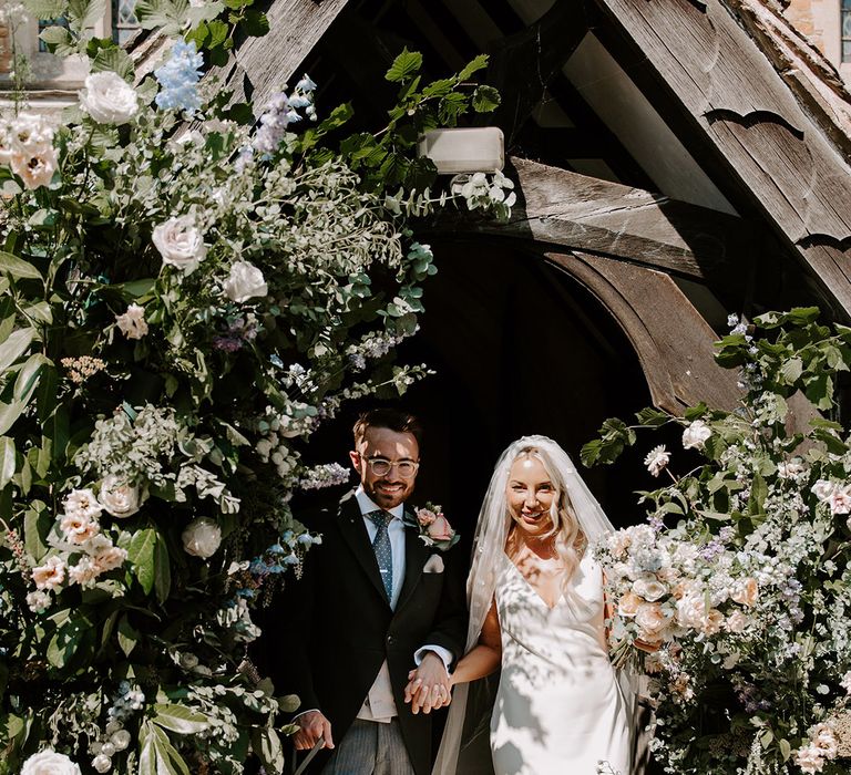 The bride and groom walk out of the church after their ceremony in between two flower columns 