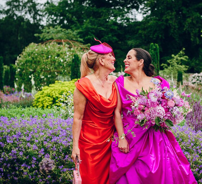 Mother of the bride in burnt orange off the shoulder cowl neck satin dress and bride in off the shoulder front ruching pink Vivienne Westwood wedding dress smiling at Middleton Lodge wedding venue