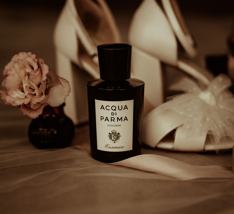 Acqua Di Parma perfume in dark bottle next to dried pink rose and strappy open toe wedding heels with large polka dot bow on the front