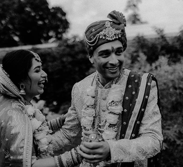 Bride & groom wear matching lei's and laugh with one another outdoors in black & white image