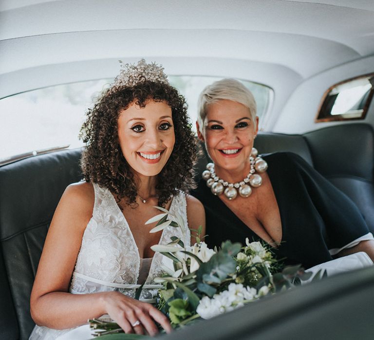 Black bride wears bridal crown in her naturally curly hair and sits beside her mother 