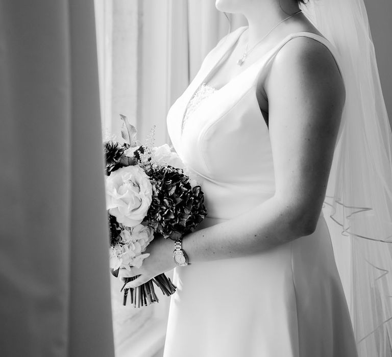 Bride in fitted wedding dress in a white lace insert with pearl earrings holing winter flower bouquet 