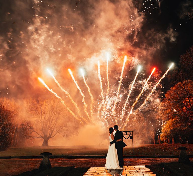 The bride and groom embrace each other as they turn to look at the fireworks 