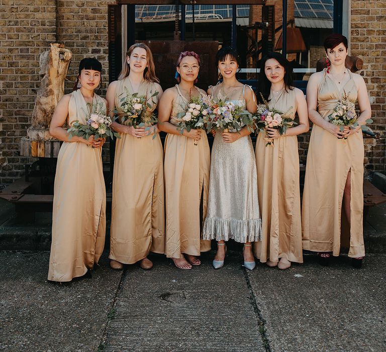 Bride stands with her bridesmaids wearing gold bridesmaid dresses with halter neck style