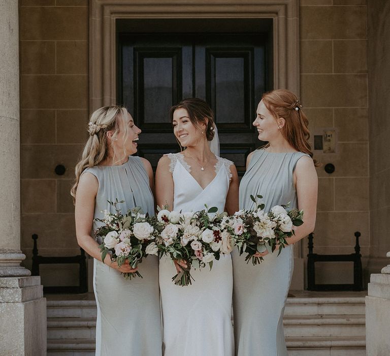 Bride stands in the middle of her bridesmaids wearing high neck sage green bridesmaid dresses holding classic bridal bouquets