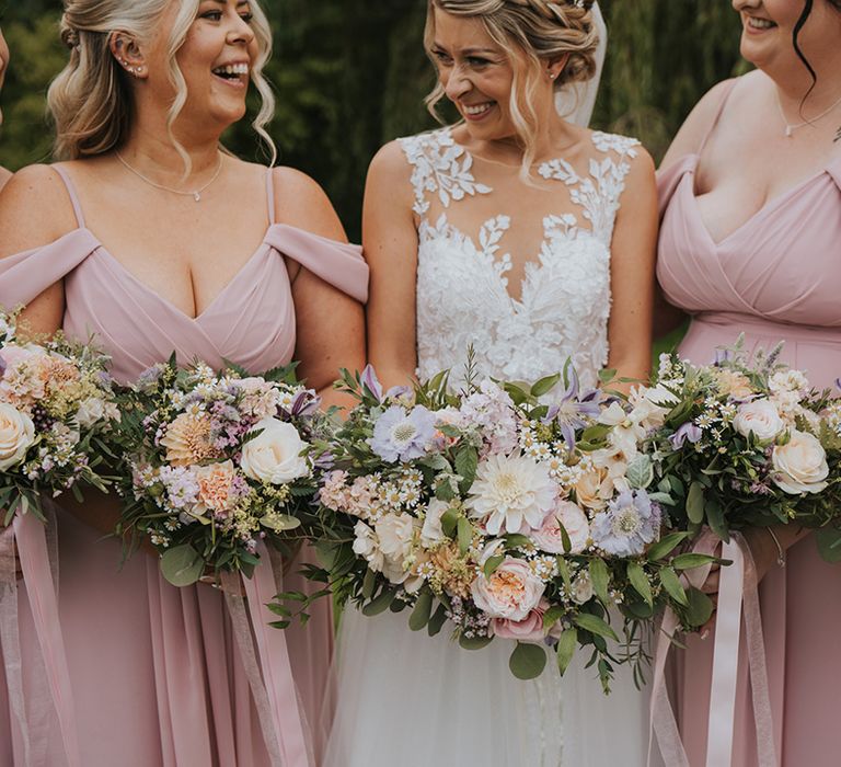 Bridesmaids in pink off the shoulder bridesmaid dresses with the bride in lace wedding dress holding pastel wedding bouquet 