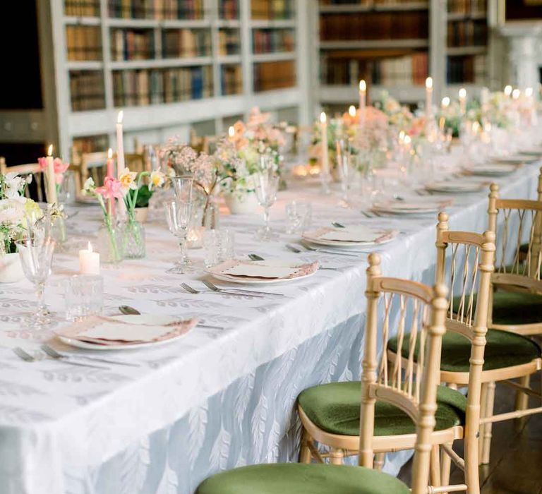 Velvet green wooden chairs at classic wedding tablescape with white tablecloth, tapered candles and spring floral arrangements in glass vases 