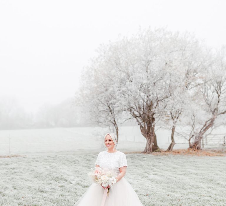 Bride in beaded sparkly top with a tulle bridal skirt holding a pink and white flower bouquet with pink ribbon for winter wedding 