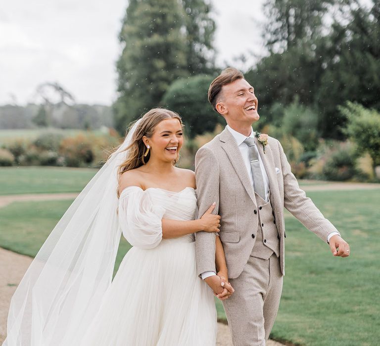 Bride in whimsical wedding dress by Watters walking along with the groom in a houndstooth suit 