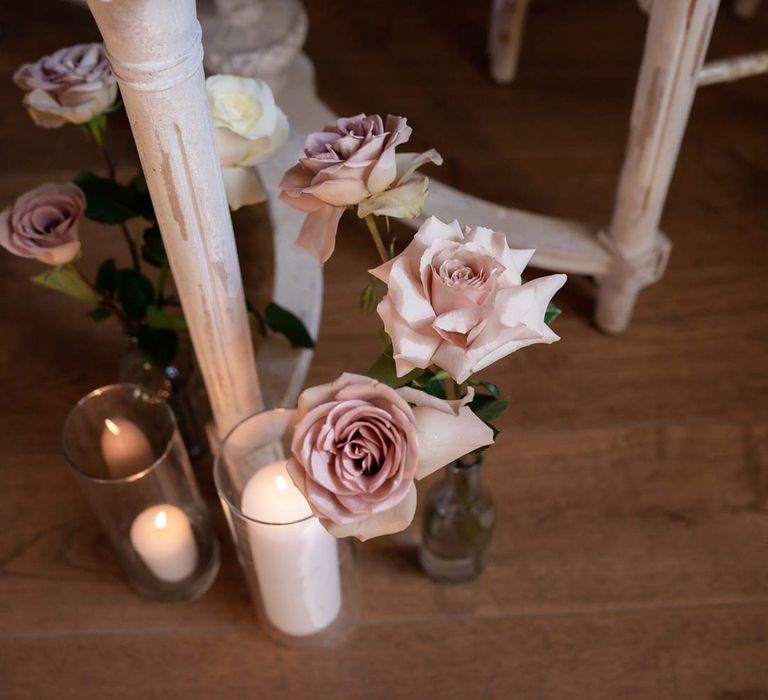 Blush garden rose flower arrangements in clear vases by large pillar candles in glass candle jars 