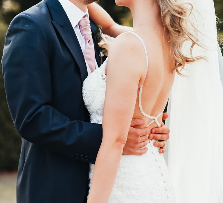 Bride in open back wedding dress with sparkly and button back detail being embraced by the groom 