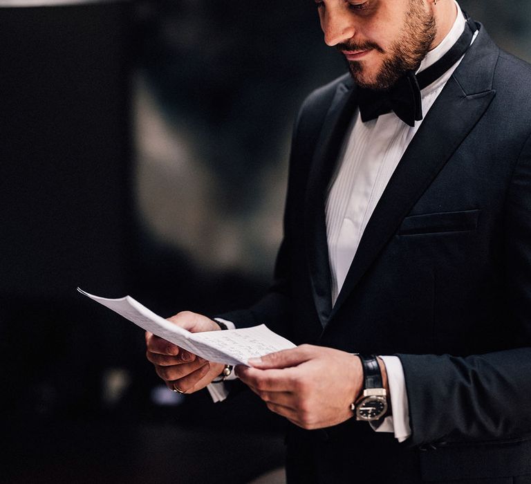 Groom in black tuxedo for traditional and modern wedding looking over his wedding speech the morning of the wedding 