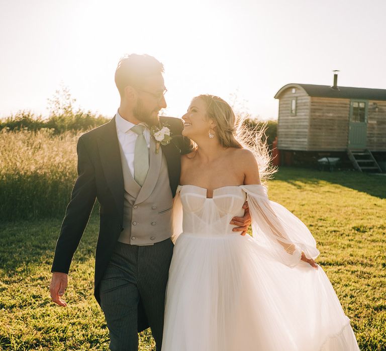 Golden hour sunset couple portrait of the bride in a tulle wedding dress walking with the groom in a morning suit for barn wedding 