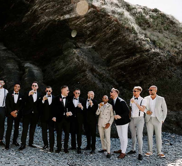 Grooms party wearing classic black-tie tuxedos, deep navy suits, and cream suits, bow ties and grooms sunglasses on Tunnels Beaches