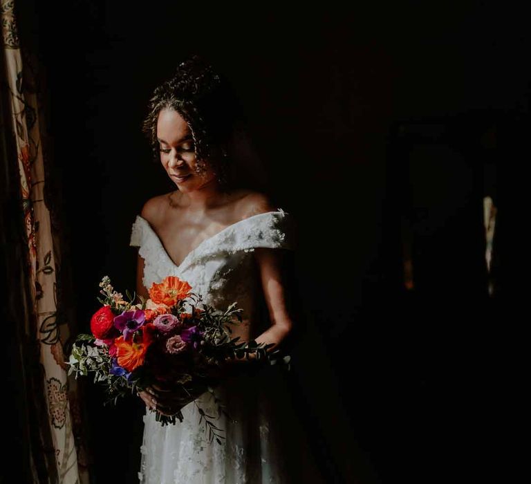 Bride in Suzanne Neville off shoulder 3D floral applique wedding dress holding spring floral bouquet at Elmore Court Gloucestershire