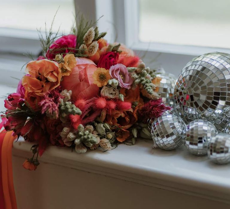 Wedding bouquet with pink and orange poppies, garden roses, carnations, dried flowers and foliage next to disco ball wedding decor 