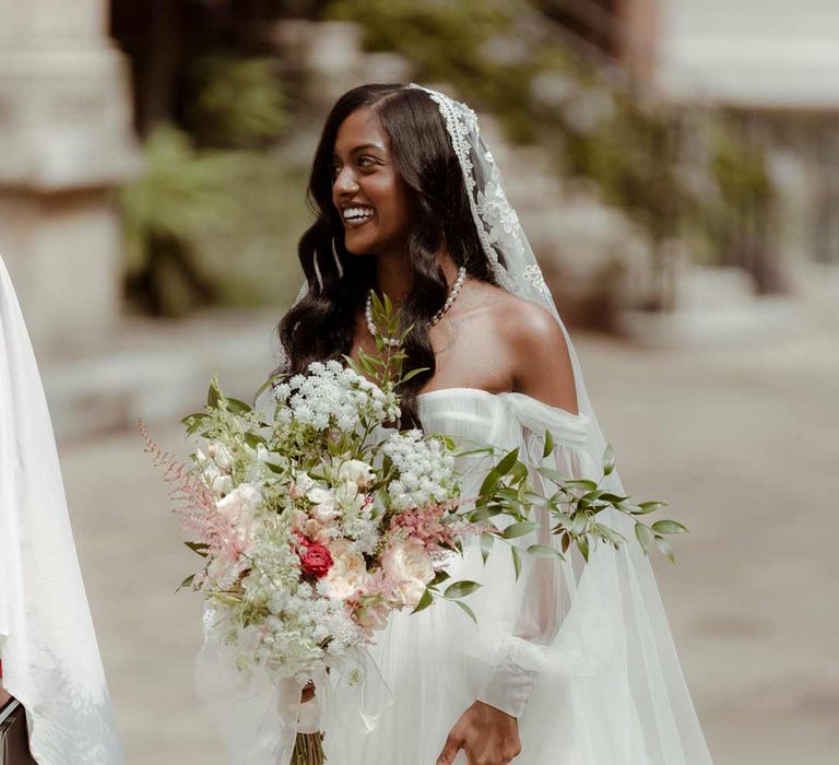 Bride in off the shoulder layered tulle wedding dress and floral embroidered cathedral-length veil holding large chic mixed flower and foliage bridal bouquet 