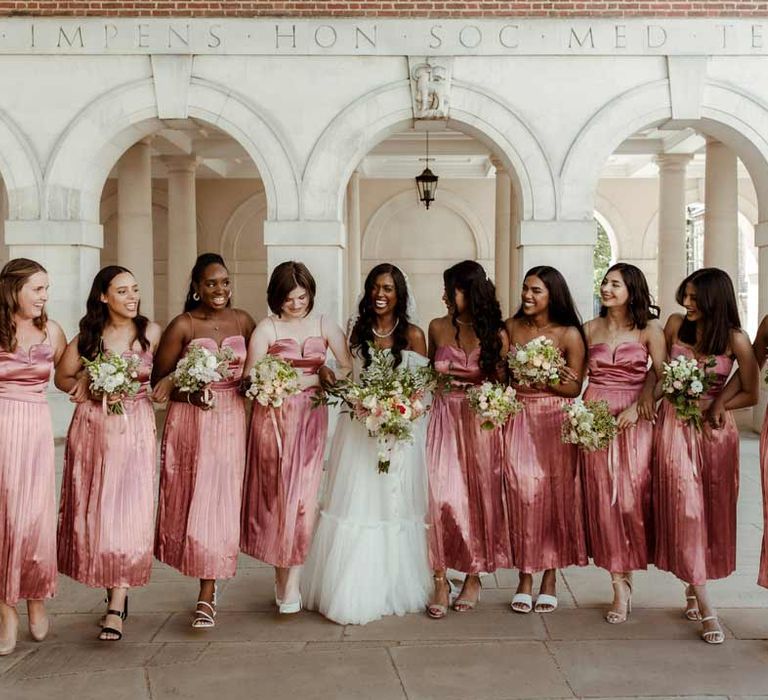 Bride in off the shoulder layered tulle wedding dress standing with bridesmaids in strappy pink midi bridesmaid dresses 