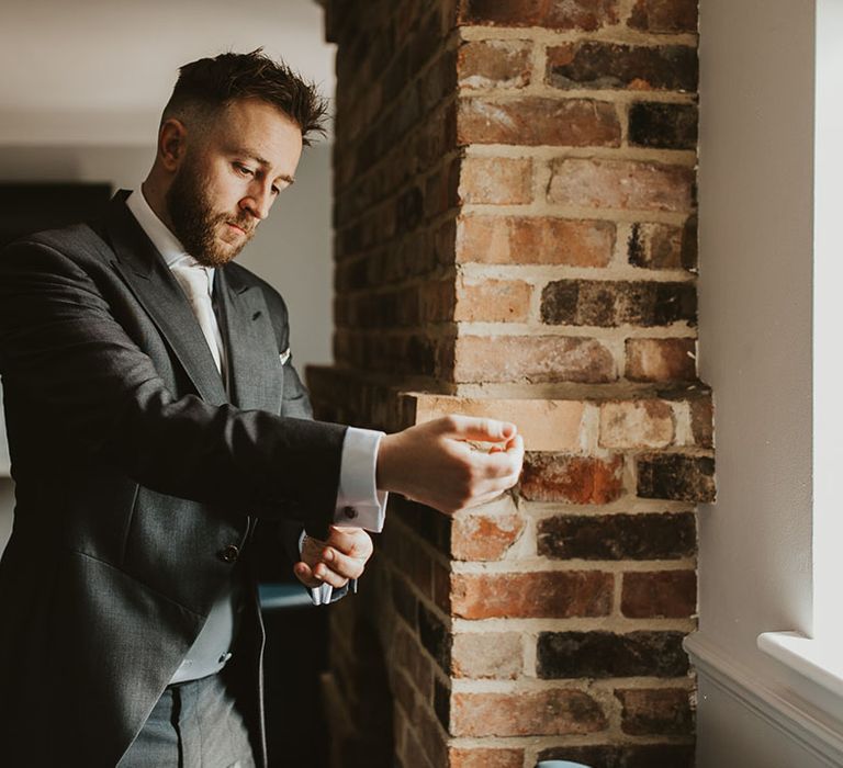 Groom in a traditional morning wedding suit with grey waistcoat putting on his cufflinks 