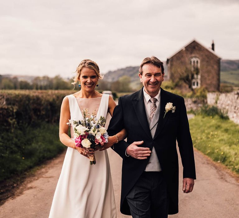 Father of the bride in a grey and black morning suit walking with the bride to the church 