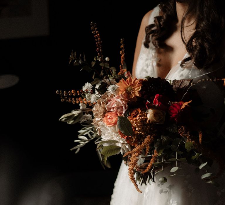 Bride in lace wedding dress at autumn wedding carrying pretty moody dark wedding bouquet 