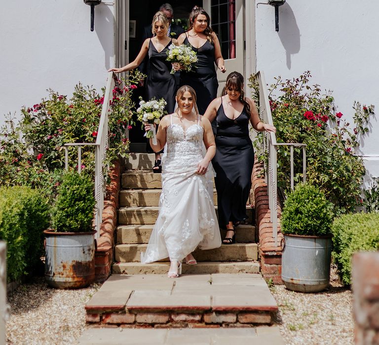 Bridesmaids in black satin bridesmaid dresses walking with the bride to the ceremony 