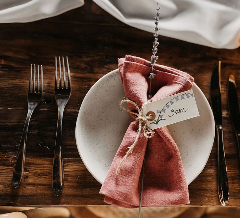 Wedding table place setting with white plate decorated with pink napkin and handwritten place name card 