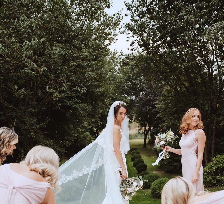 Bride wearing cathedral length embroidered edge veil in elegant satin slip wedding dress surrounded by bridesmaids in pink dresses 