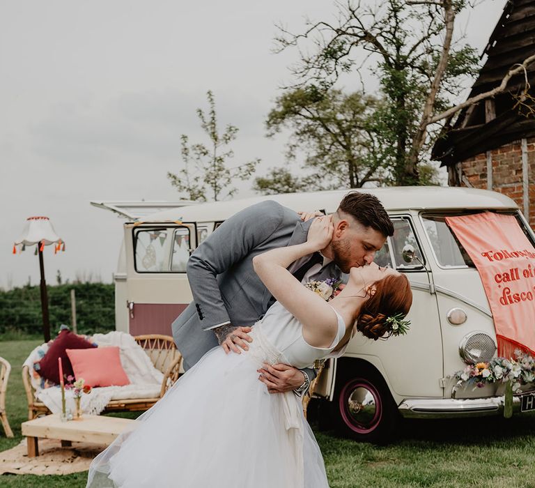 Bride in knee length wedding dress with the groom as they share a kiss in front of the retro wedding banner 